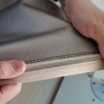 Hands of male leatherworker holding piece of leather with zipper by machine