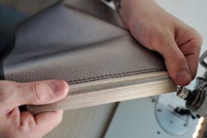 Hands of male leatherworker holding piece of leather with zipper by machine