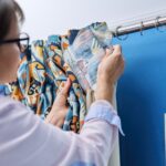 Woman hanging velvet curtains on metal hooks on cornice pipe
